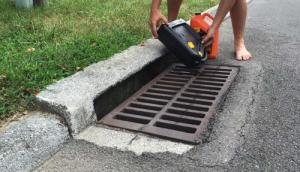 Man dumping chemicals into a storm drain along a curb in the road.
